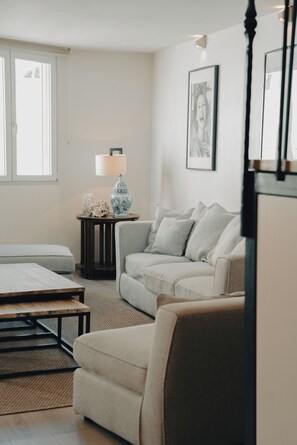 Una sala de estar con un sofá, una silla, una mesa, una lámpara y un cuadro en la pared.