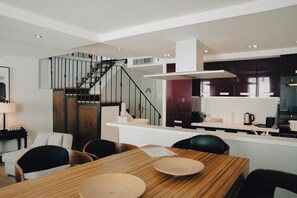 Una cocina moderna con armarios oscuros, una isla central y un comedor con mesa y sillas de madera.