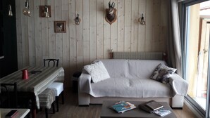 Ein gemütliches Wohnzimmer mit Holzwand, einer Couch, einem Esstisch mit Stühlen und einem Couchtisch mit Büchern und einem Telefon.