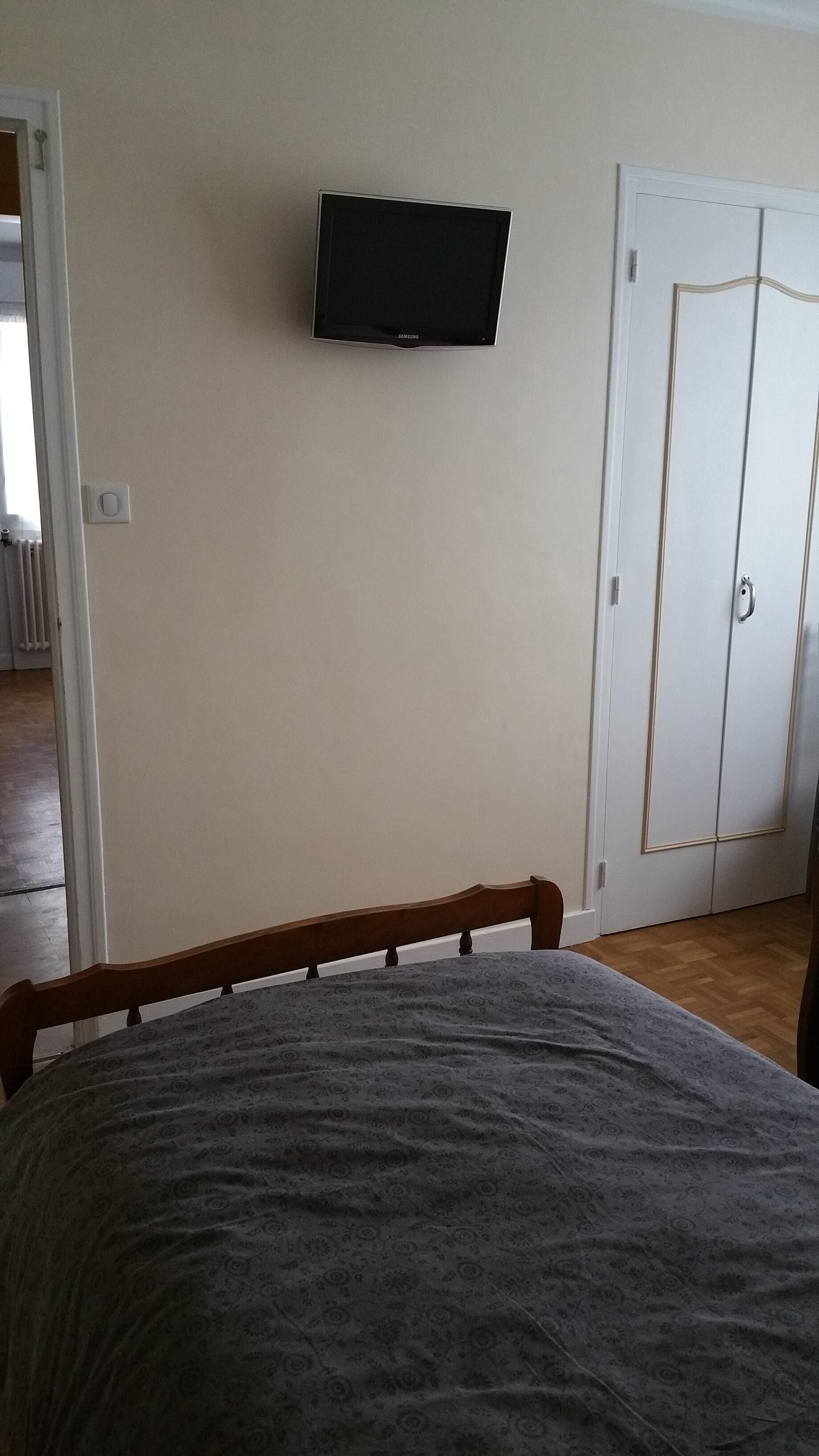 Un dormitorio con cama, televisión montada en la pared y armario.