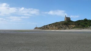 A beach with a small building on a hill, a lighthouse in the distance, and a clear sky. - House / Villa - MORIEUX (Morieux)