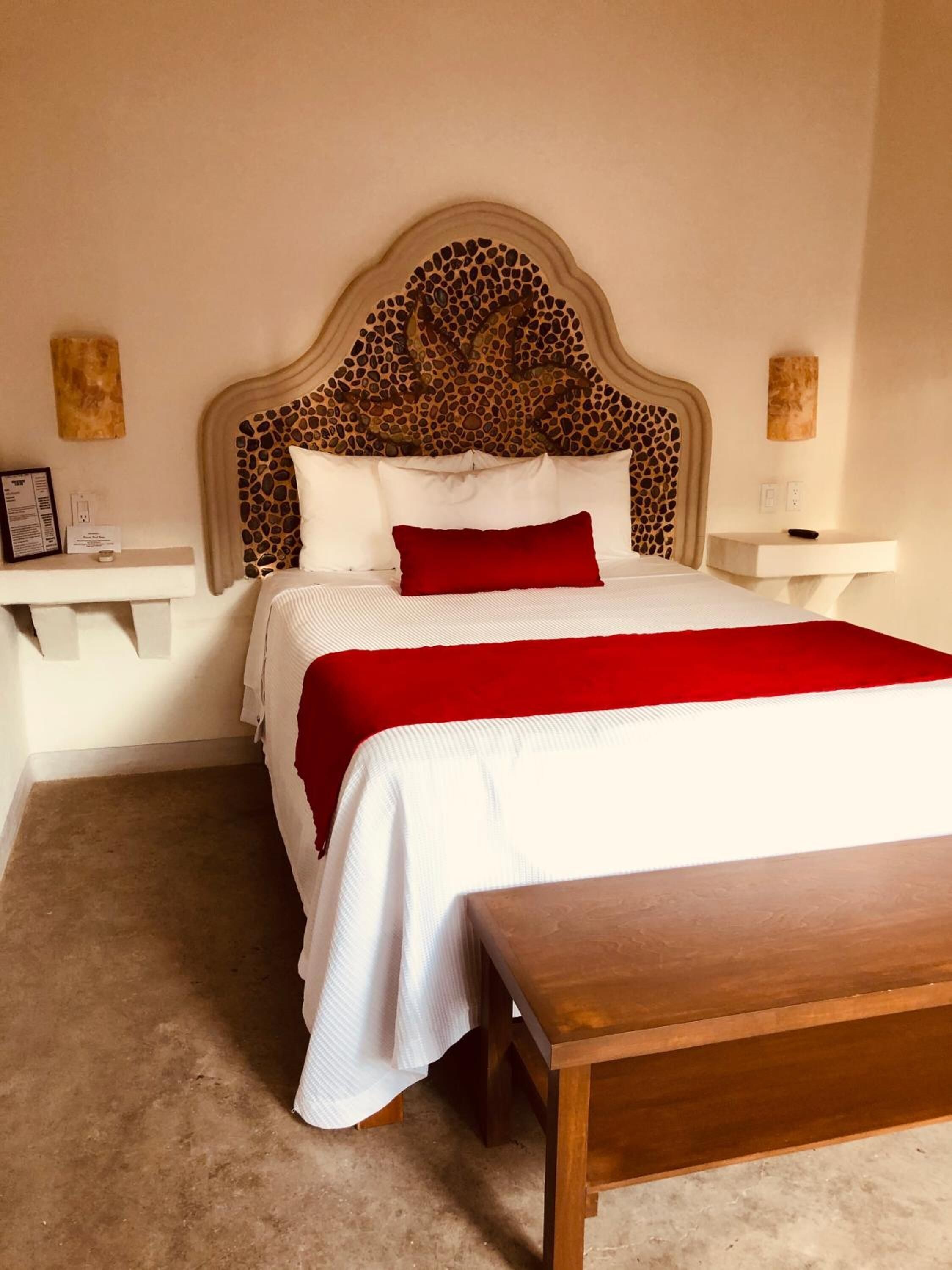 Una camera d'albergo ordinata con un letto grande, un comodino in legno e una coperta rossa.