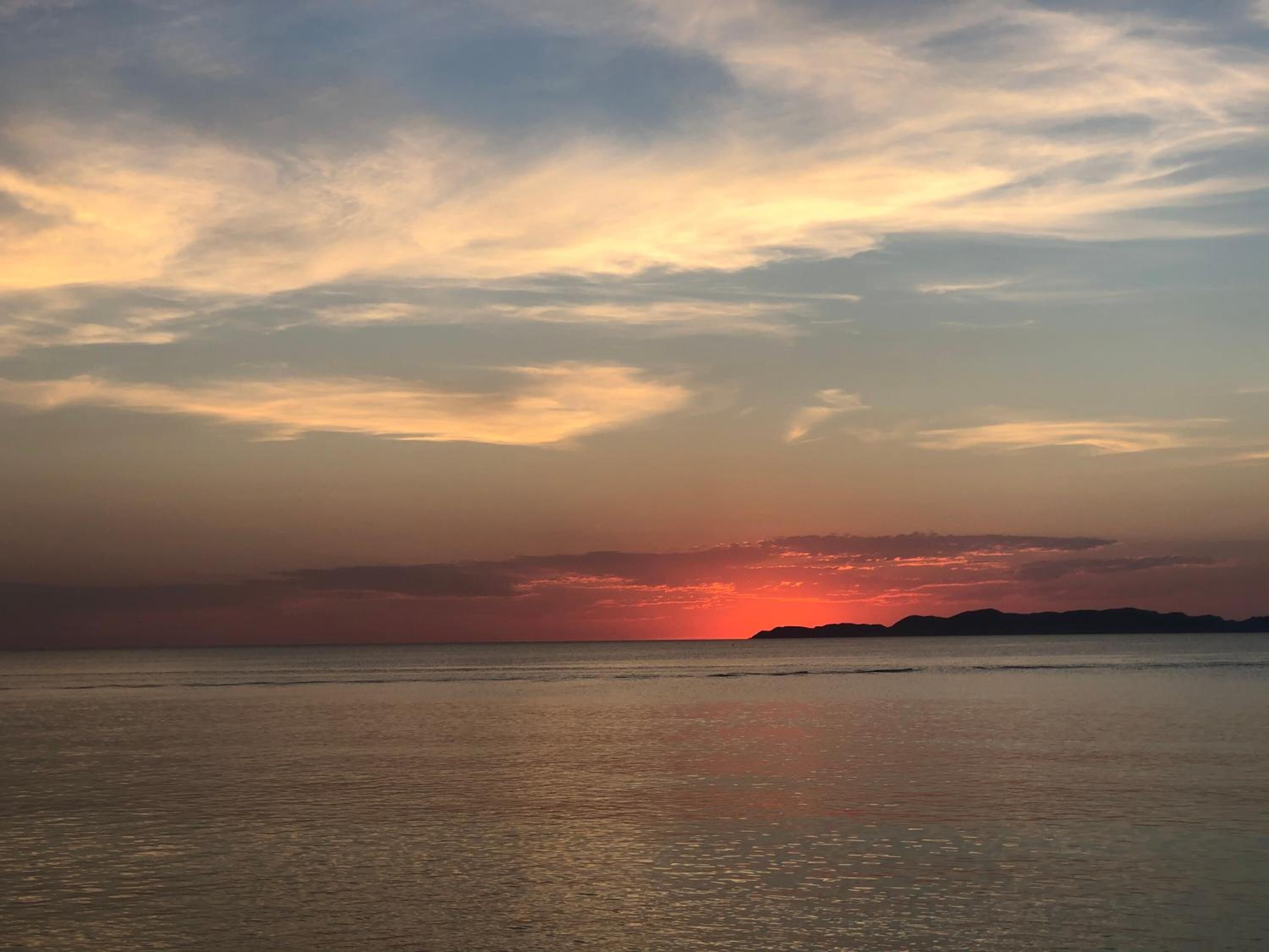 A sunset over a calm sea with distant land silhouettes.