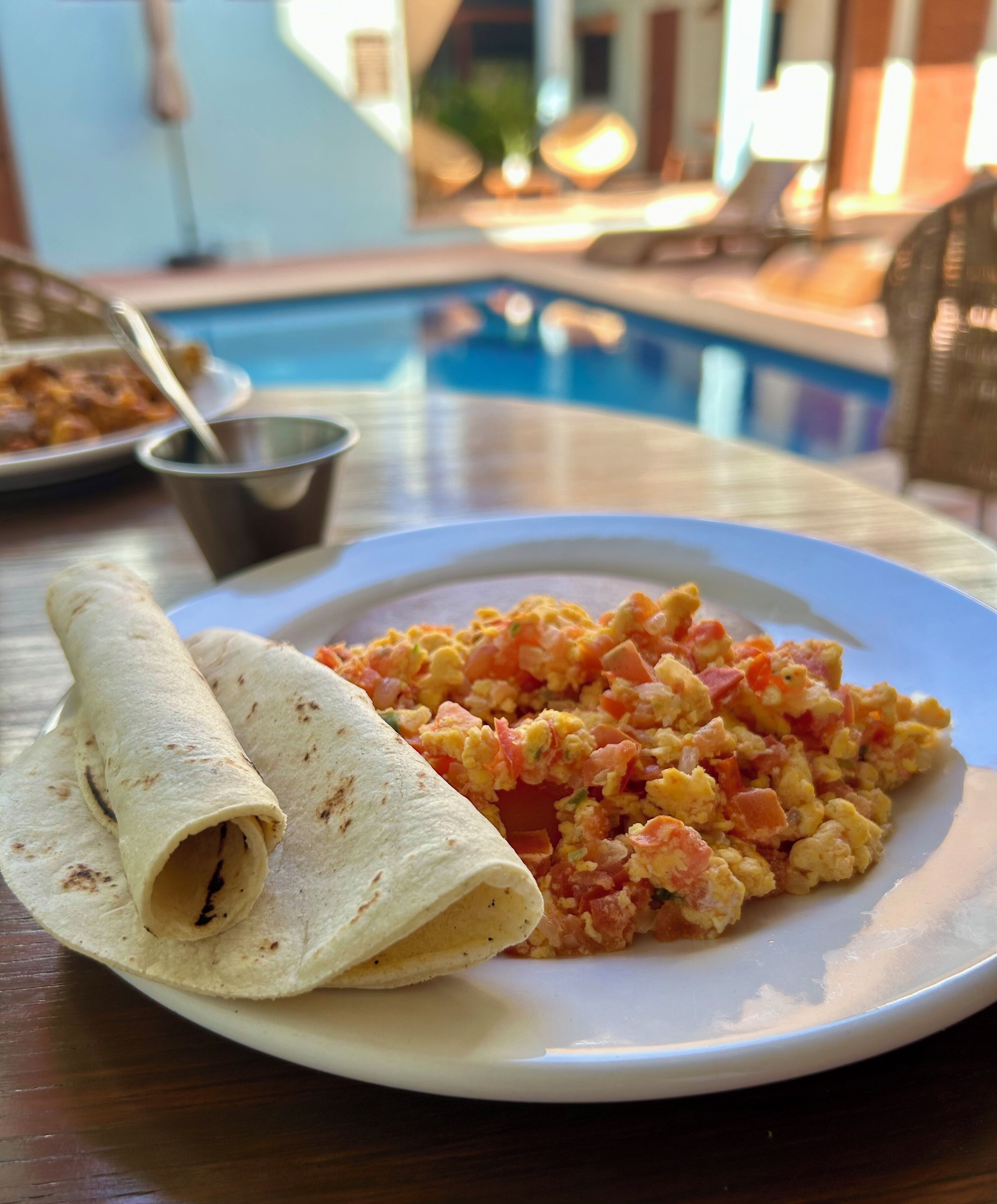Ein Teller mit Rührei und einer Tortilla auf einem Tisch in der Nähe eines Pools.