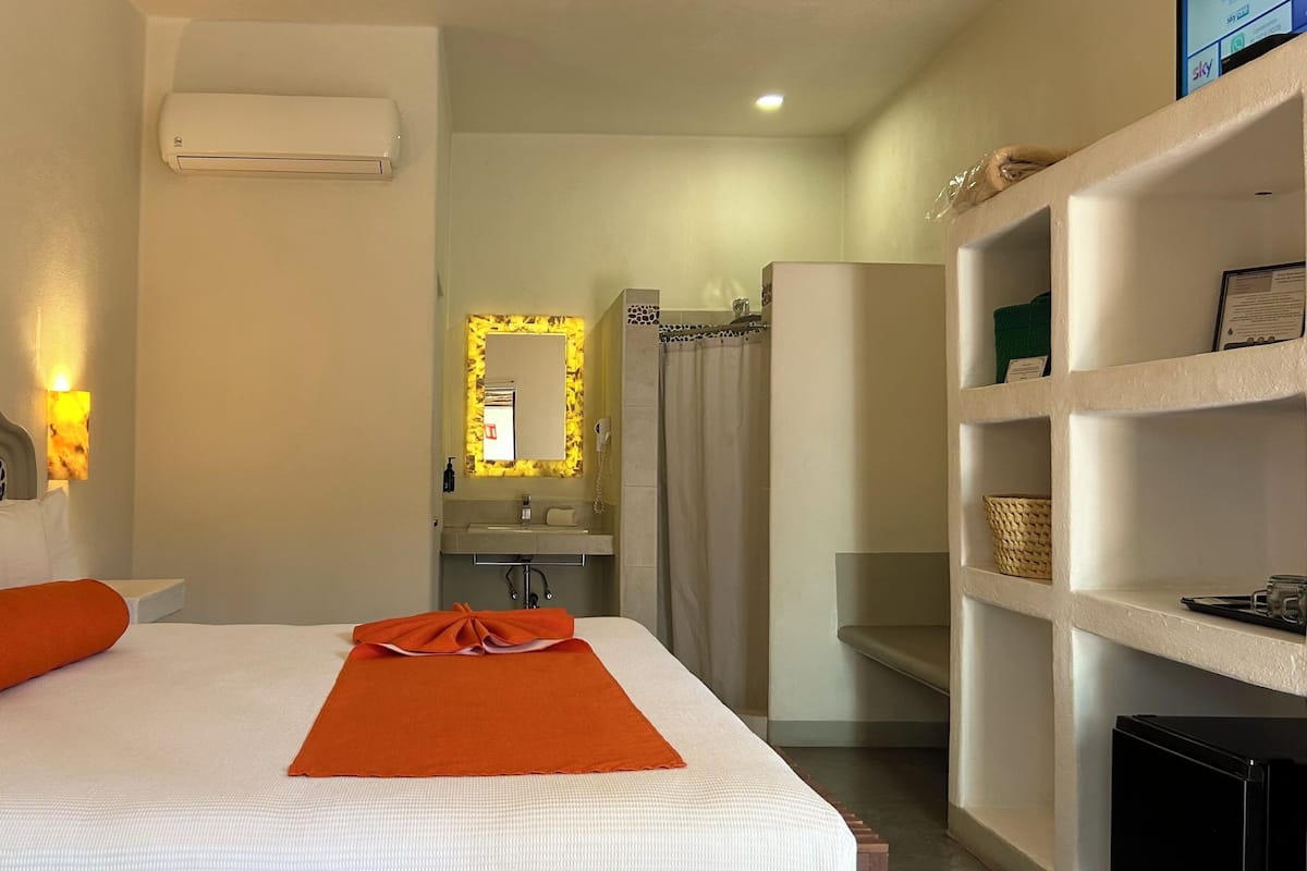 A hotel room with a bed, a bathroom, and a shelf unit.