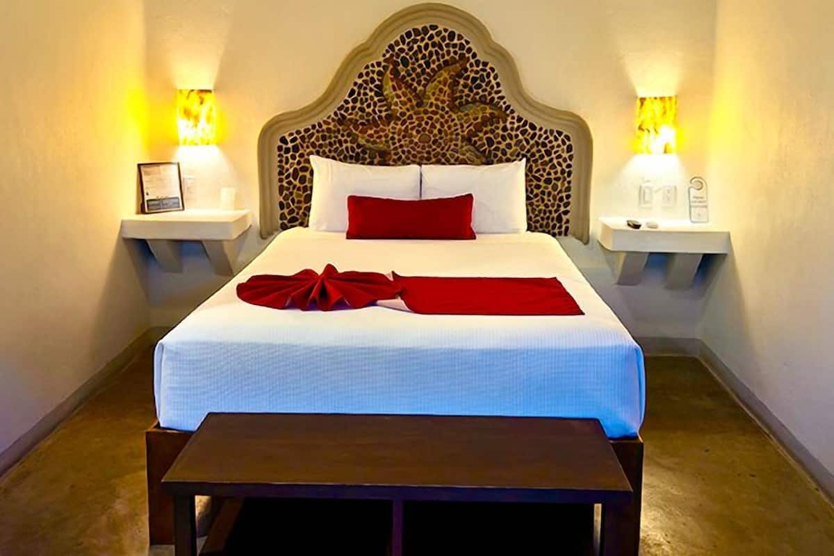A hotel room with a bed, two bedside tables, a bench, and a unique headboard.