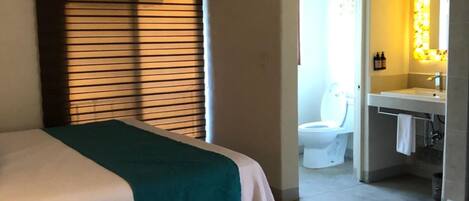 A hotel room with two beds, a ceiling fan, an air conditioning unit, a bathroom with a toilet, and a sink.