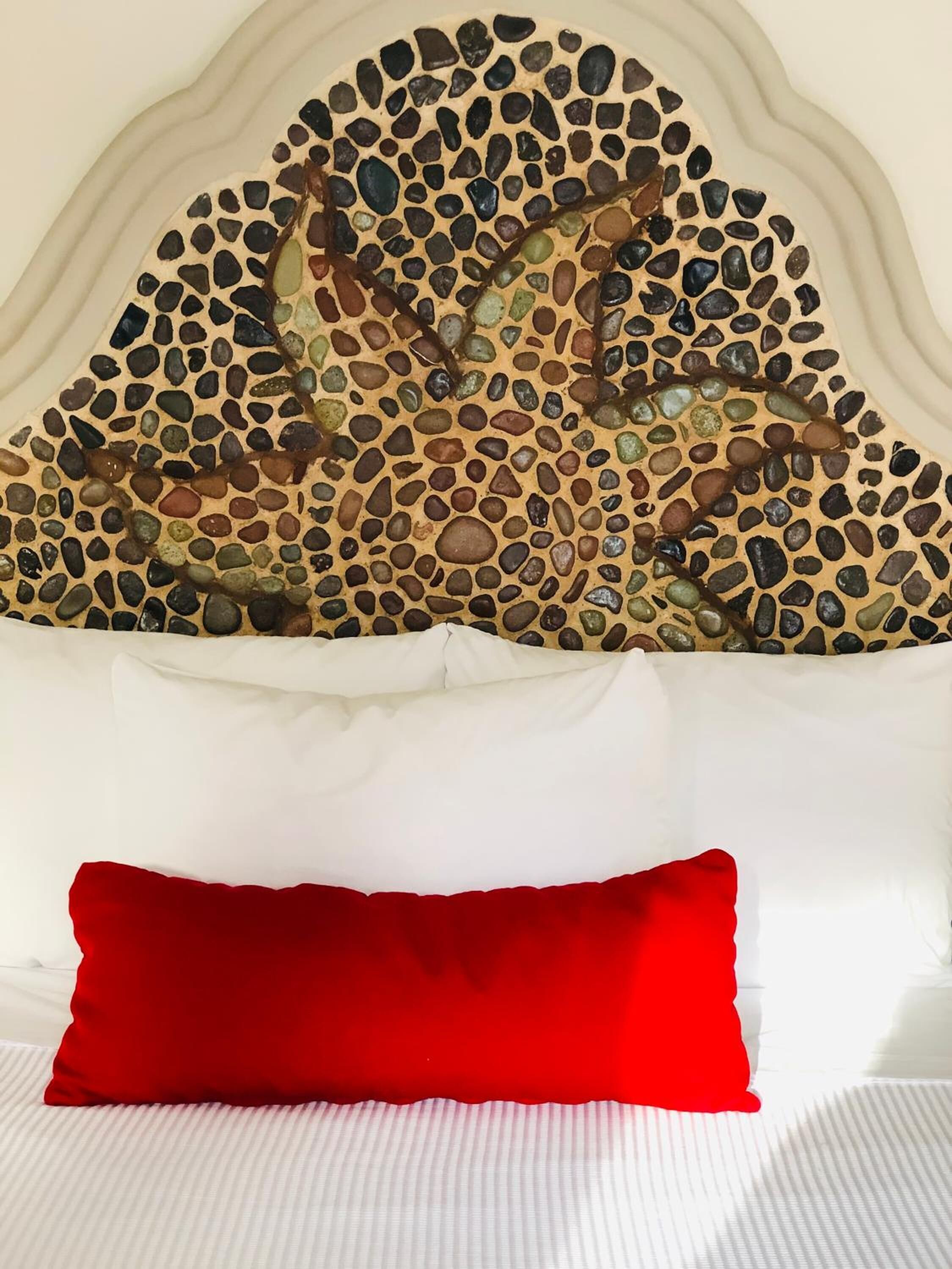 Ein Bett mit weißem Kopfteil und einem roten Kissen.