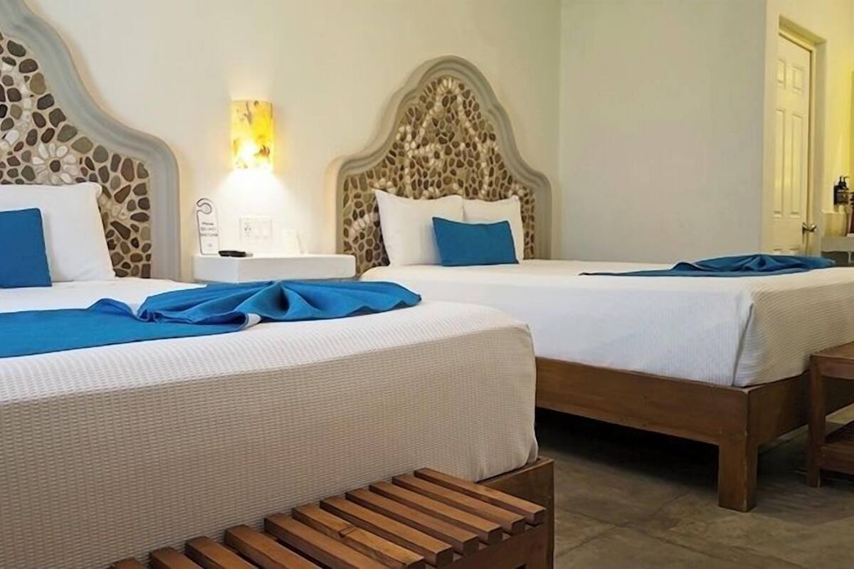 Two beds with headboards, a nightstand, a wooden bench, and a wall with a mosaic pattern.