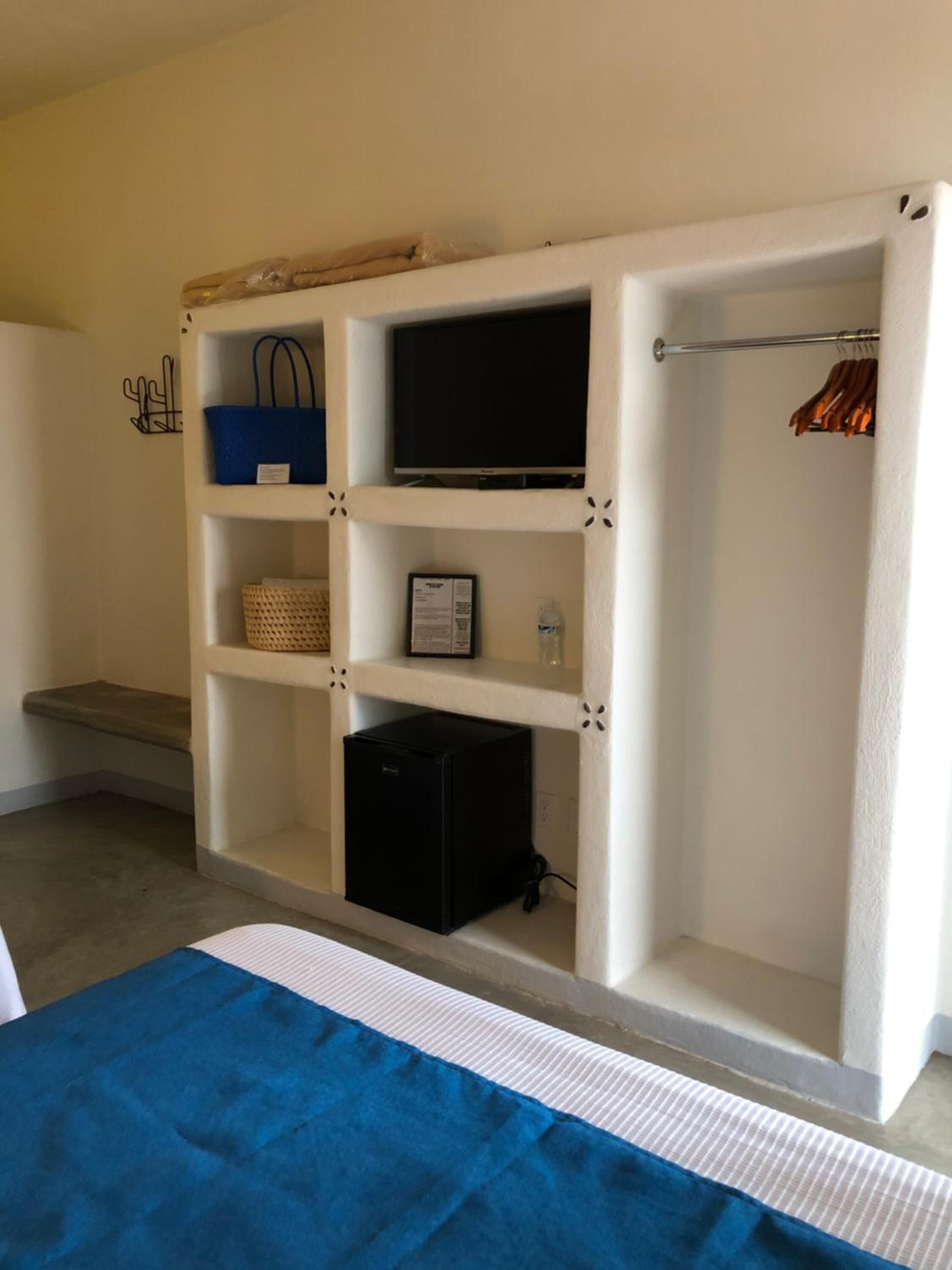 A room with a white built-in wardrobe, a flat-screen TV, a small black refrigerator, and a blue bedspread.