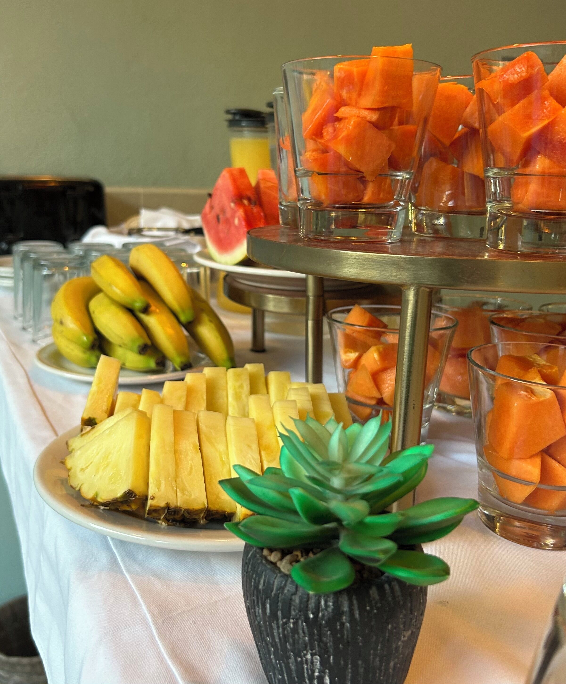 A buffet table with fruit options including bananas, pineapple, and cantaloupe.