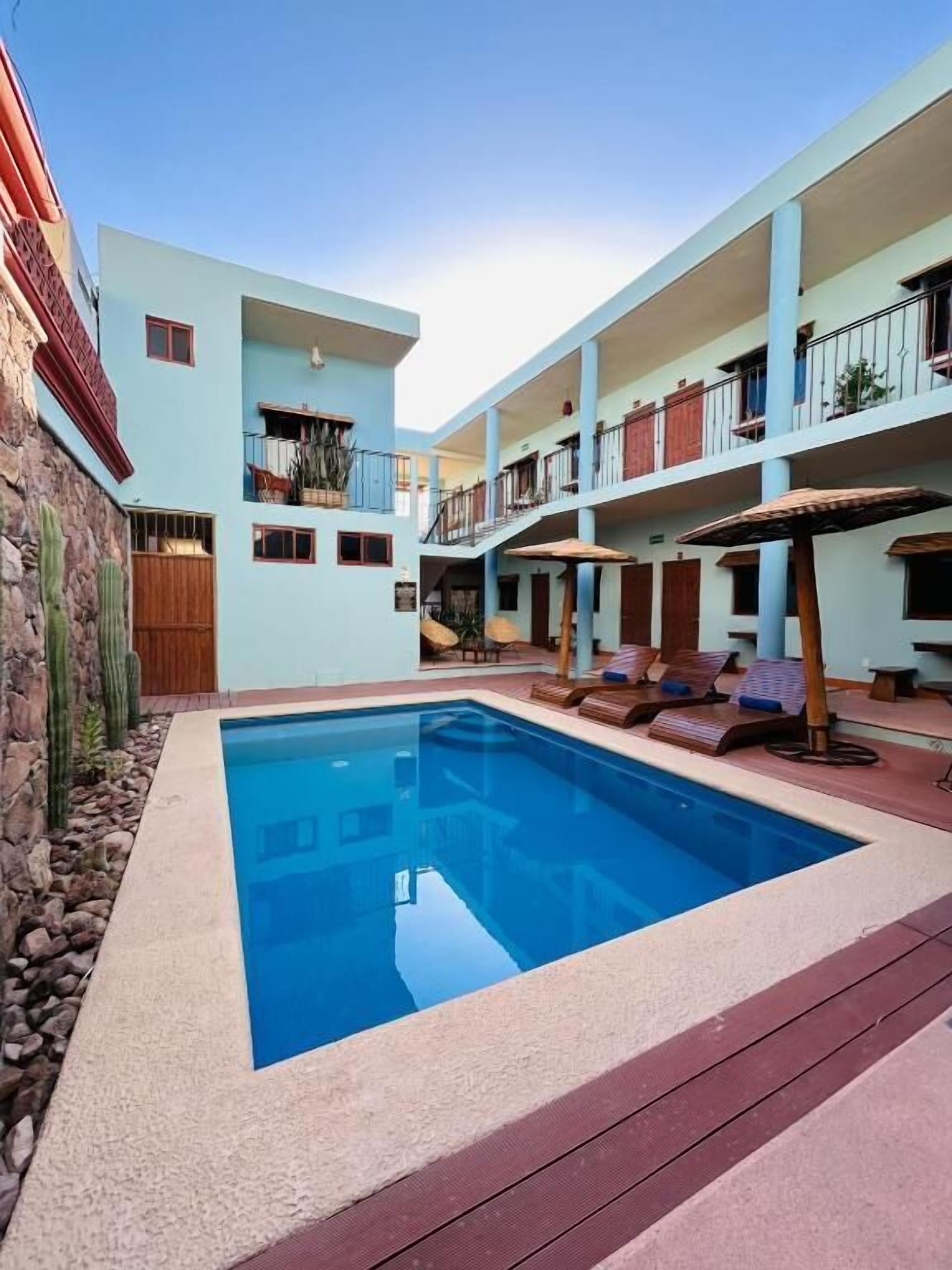 Ein Poolbereich mit einem kühlen, blauen Pool, umgeben von einem hellblauen Gebäude mit Balkonen und einer Steinmauer.