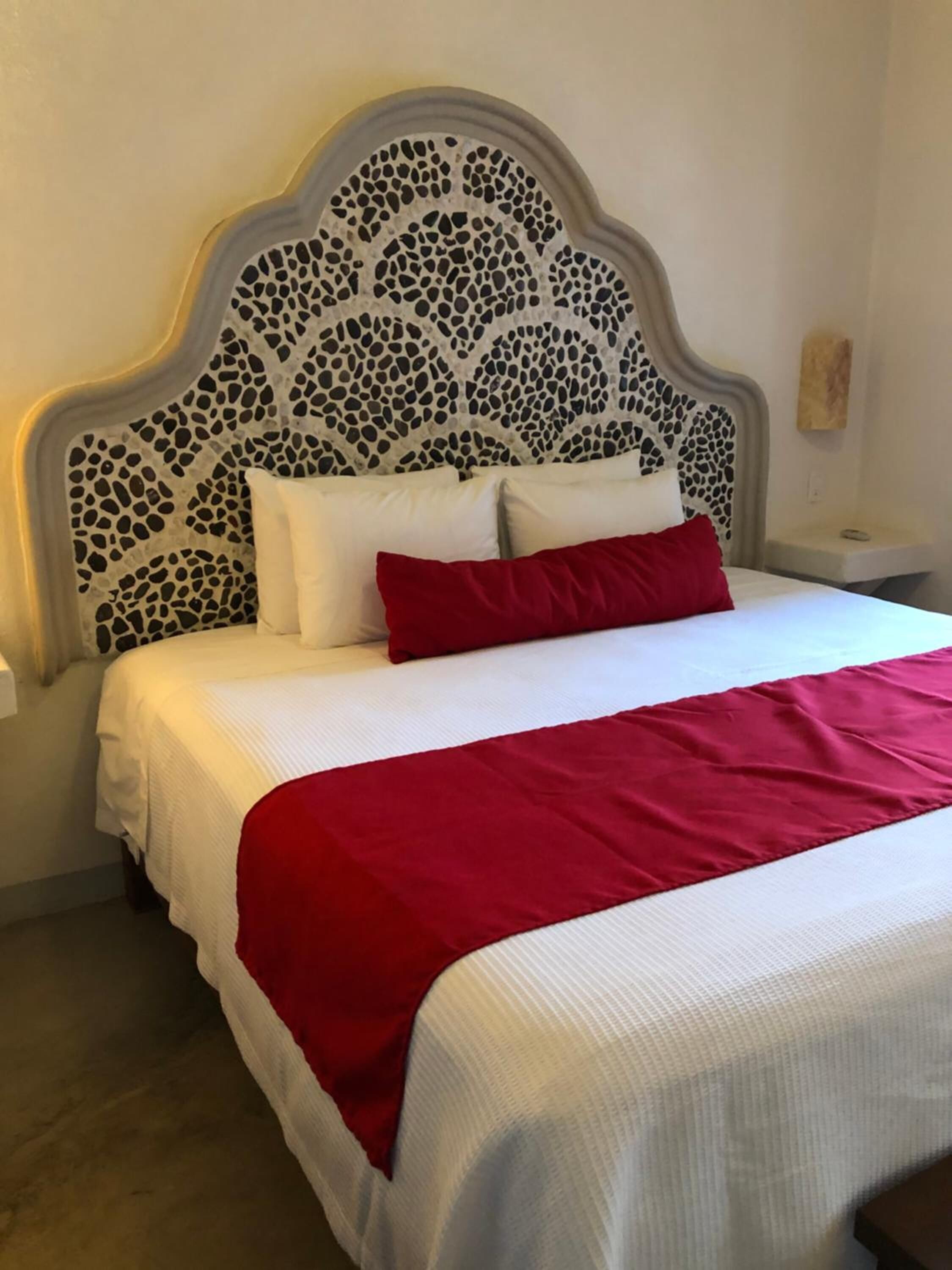 Una cama con una colcha blanca y roja, un cojín rojo y un cabecero con un diseño de mosaico.