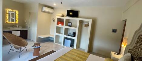 Quarto de hotel com cama, cadeira, escrivaninha, guarda-roupa e ventoinha no teto.