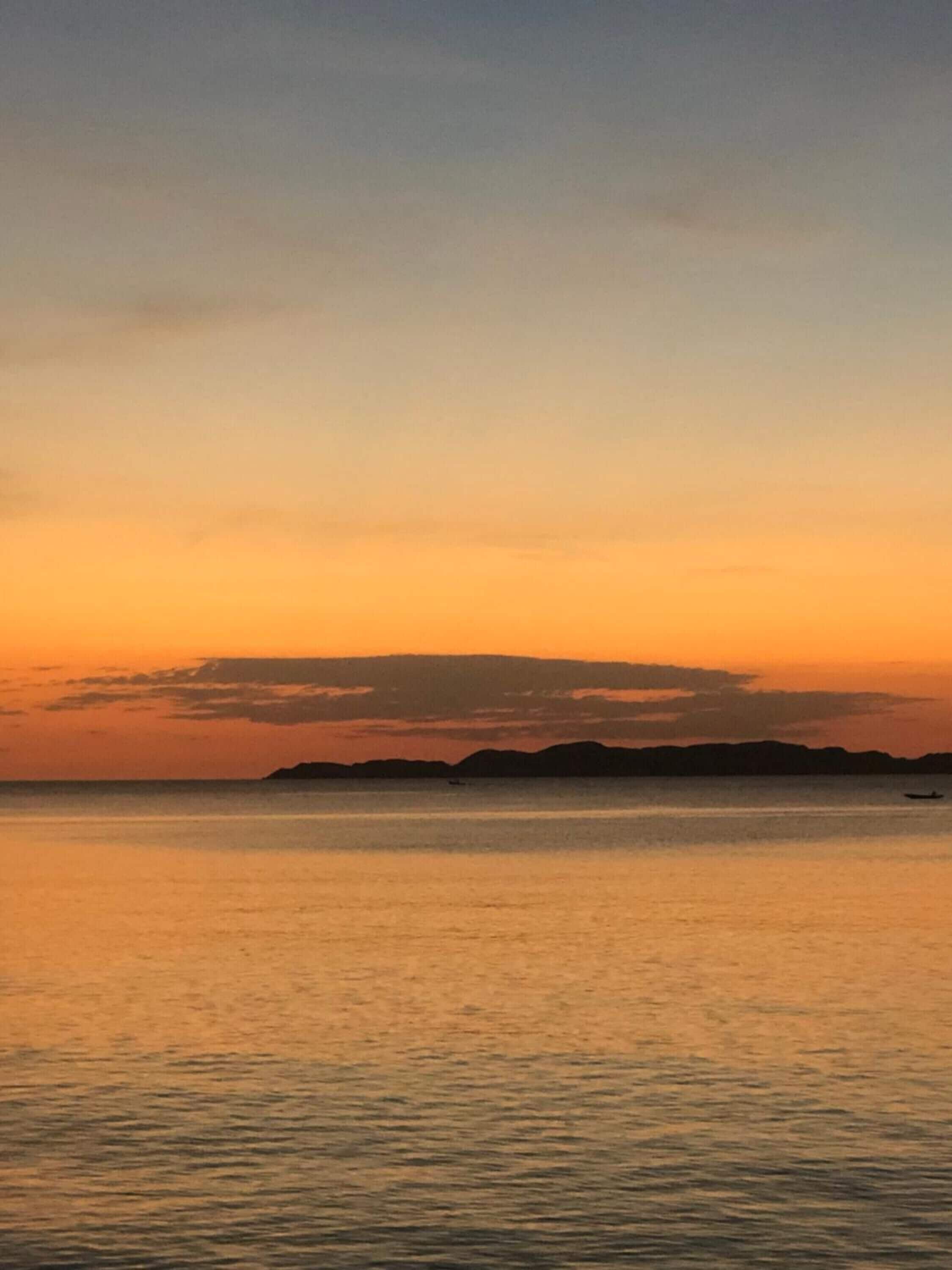 A sunset over a calm sea with distant landforms.