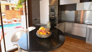 A modern kitchen with stainless steel appliances, a dining table with a fruit bowl, and a view of a swimming pool through glass doors. - FANTASTIC SEA VIEWS  (Lloret de Mar)