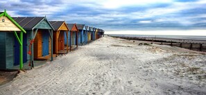 Une rangée de cabanes de plage s’étend le long d’une plage de sable, offrant une vue sur la mer.