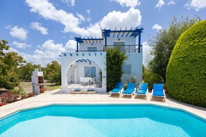 A pool area with a pergola, lounge chairs, and a clear blue sky.