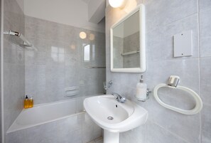 A modern bathroom with a bathtub, a sink, a mirror, and toiletries.