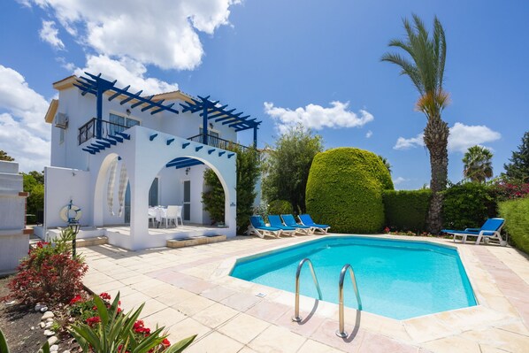 A pool area with a clear blue pool, lounge chairs, and a covered seating area with a pergola.