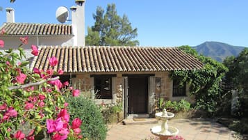 A stone house with a tiled roof, a satellite dish, and a garden with a fountain.
