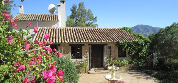 A stone house with a tiled roof, a satellite dish, and a garden with a fountain.