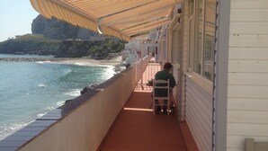 Un balcon doté d’auvents à rayures, donnant sur une zone côtière avec une falaise rocheuse.