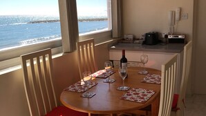 Un coin repas avec une table et des chaises en bois, une horloge au mur et une vue sur la mer par la fenêtre.