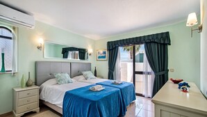 Un dormitorio con dos camas, una mesita de noche, un aparador, una ventana con cortinas y vistas al exterior.