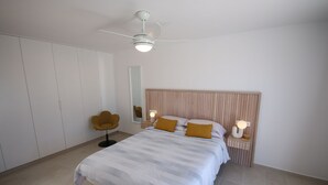 Un dormitorio con cama, mesitas de noche, una silla, ventilador de techo y armario.