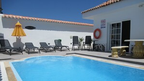 Un área de piscina con sillones de descanso y una sombrilla amarilla.