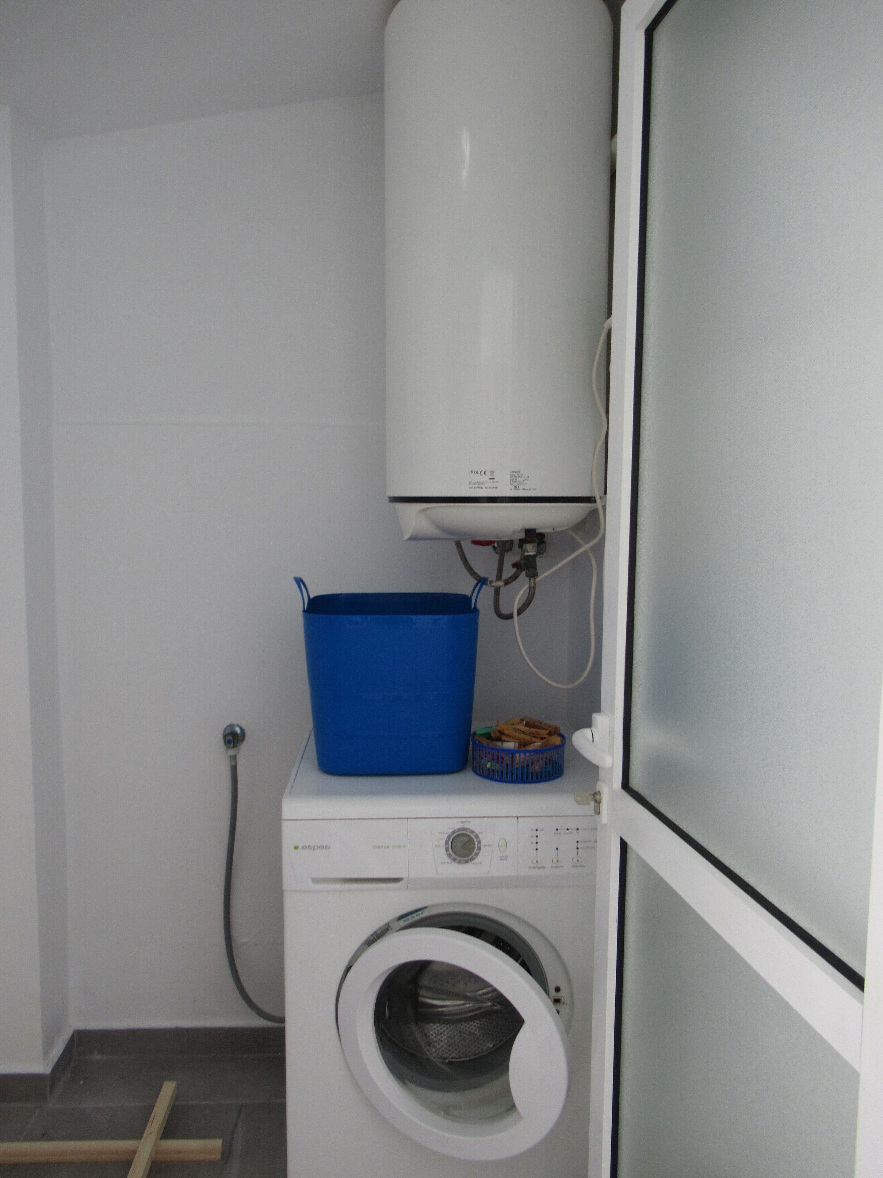 Une petite buanderie équipée d’un lave-linge à chargement frontal, d’un panier à linge bleu et d’un chauffe-eau blanc.