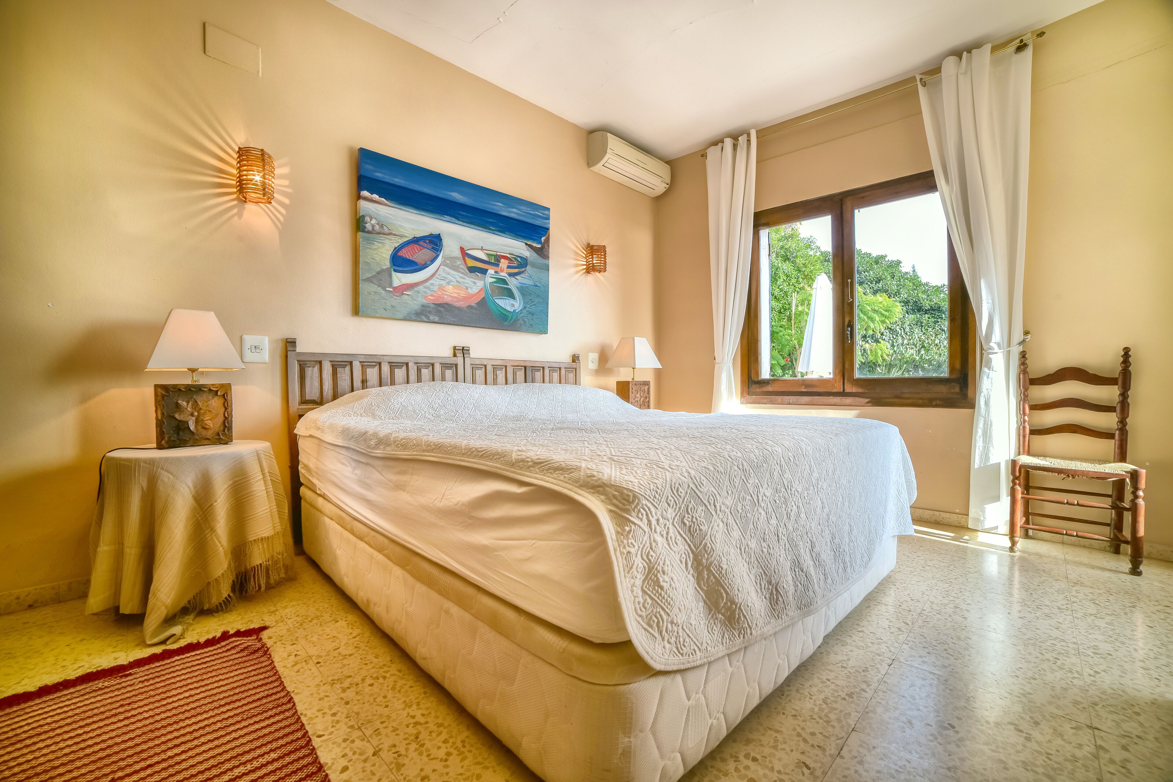 Un dormitorio con una cama grande, dos mesitas de noche con lámparas, un cuadro en la pared y una ventana con cortinas.