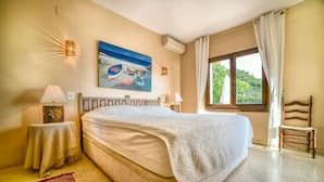A bedroom with a large bed, two bedside tables with lamps, a painting on the wall, and a window with curtains. - Family holiday house directly at sea (Calp)
