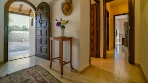 A hallway with a wooden door, a small table with a vase of flowers, and a stone wall visible through an archway. - Family holiday house directly at sea (Calp)