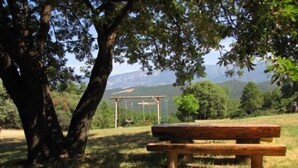 Un banc en bois, placé sous un arbre dans un parc, avec une balançoire et des montagnes en arrière-plan.