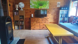Mökki, jonka sisustuksessa on puulattia, televisio, kirjahylly, työpöytä ja sänky.