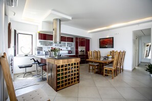 Una cocina moderna con una isla central, taburetes de bar, una bodega y un comedor con sillas de madera.