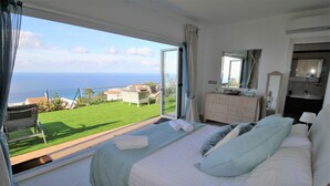 A bedroom with a large bed, a dresser, a mirror, and a view of the ocean through a sliding glass door. - New 4 bed villa in Zambrone - Spectacular 180 degree panoramic sea views. (Zambrone)