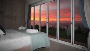 A bedroom with a bed, a view through a sliding door, and a balcony. - New 4 bed villa in Zambrone - Spectacular 180 degree panoramic sea views. (Zambrone)
