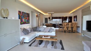 A modern living room with a sectional sofa, a glass coffee table, and a dining area with wooden chairs. - New 4 bed villa in Zambrone - Spectacular 180 degree panoramic sea views. (Zambrone)