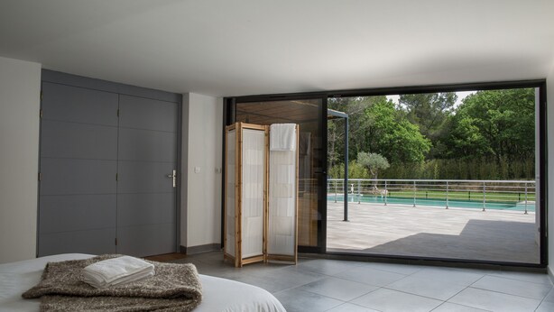 A bedroom with a bed, a grey wardrobe, and a sliding glass door leading to an outdoor area with a pool.