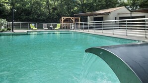 A swimming pool with a water slide, surrounded by a white fence and green lounge chairs.