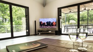 A room with a TV displaying a herd of cows, a dining table with chairs, and a book.
