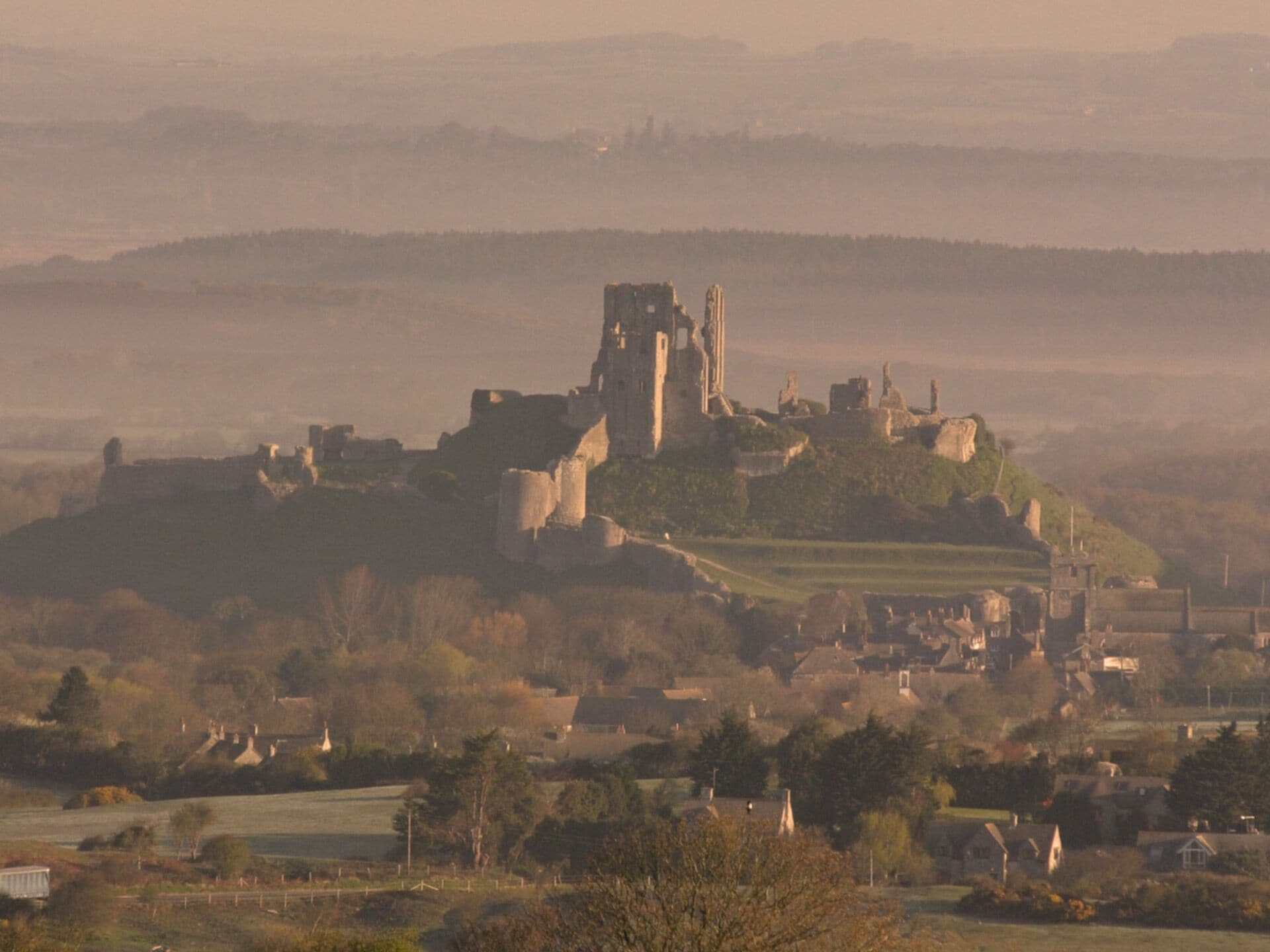 A historic castle on a hill with ruins, surrounded by a rural landscape.
