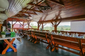 An outdoor dining area with wooden benches and tables, a ceiling with exposed beams, and a view of the landscape. - Hotel Kasztelan (Dobczyce)