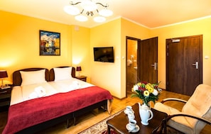 Een hotelkamer met een bed, een televisie, een bureau met een bloevas en een stoel.