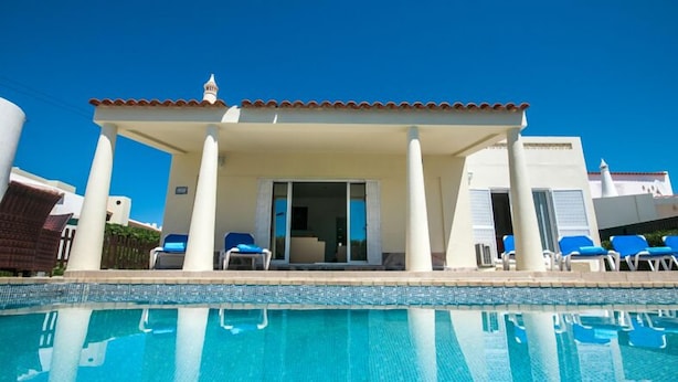 A poolside area with a covered seating area, a clear pool, and a building with columns. - Villa Sete, Beautiful Spacious Private 5 Bedroom Villa, Albufeira Town (Albufeira)