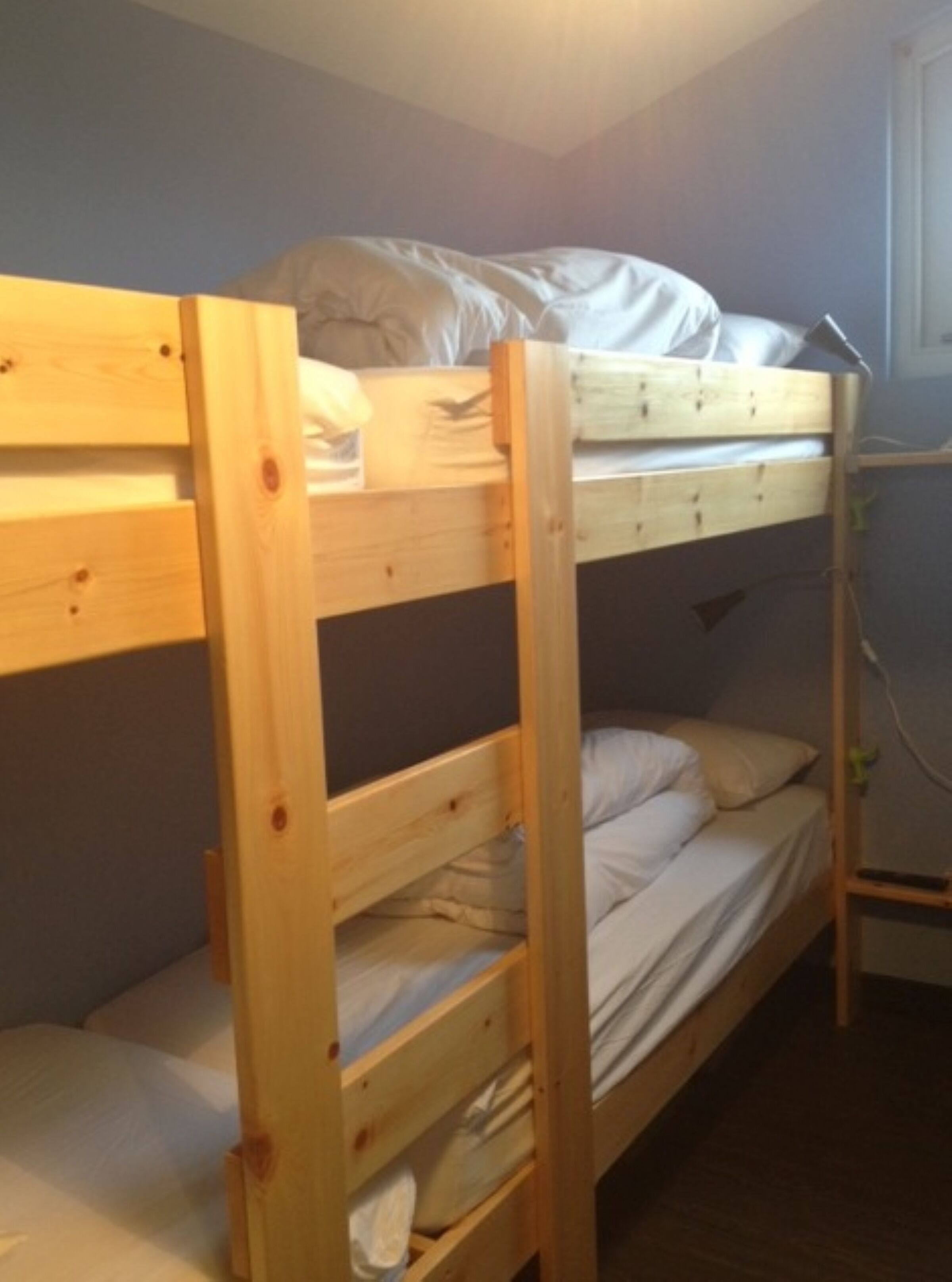 Une chambre avec un lit superposé en bois, un lit inférieur doté d’un matelas et d’oreillers, et un lit supérieur avec un oreiller et une couverture.