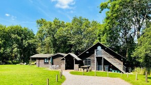A rustic lodge with a gravel driveway leading to a wooden building with a large front porch and a staircase.